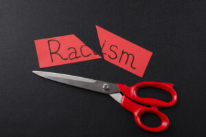 Top View Of Red Scissors And Cutted Paper Card With Word Racism On The Black Surface.concept Of Stop Racism