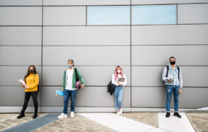 Young Students With Face Mask In Casual Clothes Standing In Front Of A Grey Wall Background New Normal Concept With People Going To School